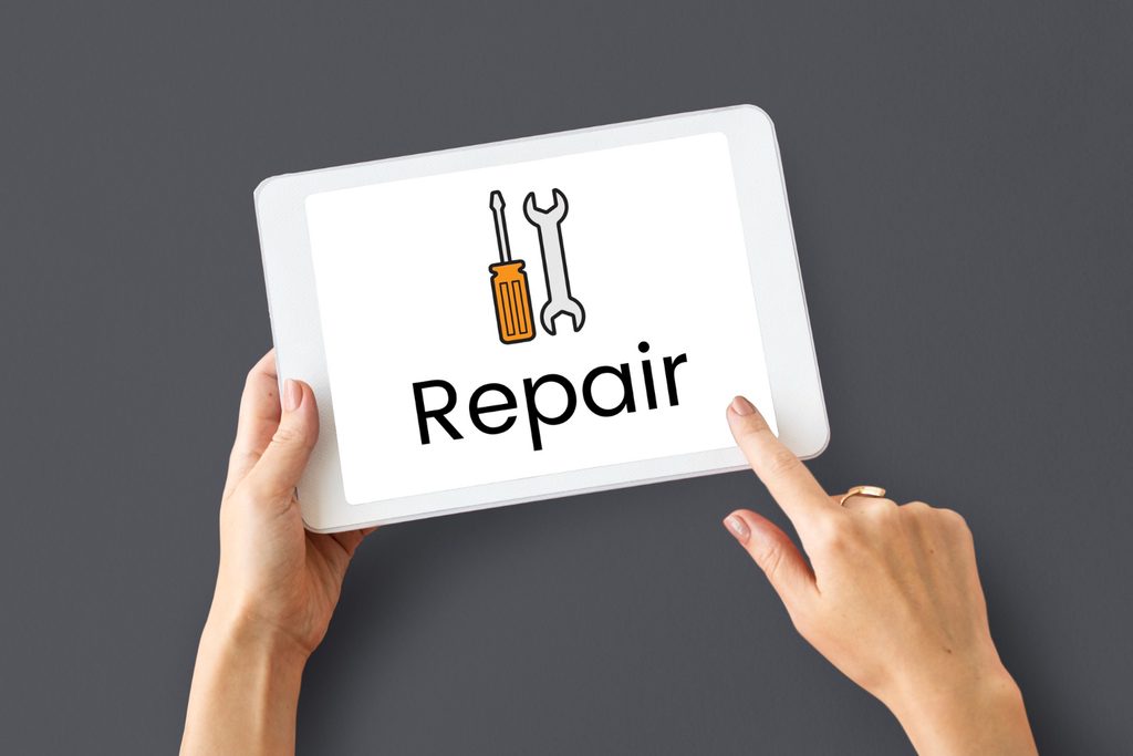 Inward Processing Unipac Shipping Tablet held by two hands showing the word “repair” with a screwdriver and wrench icon above it, on a dark background, conveying repair service.